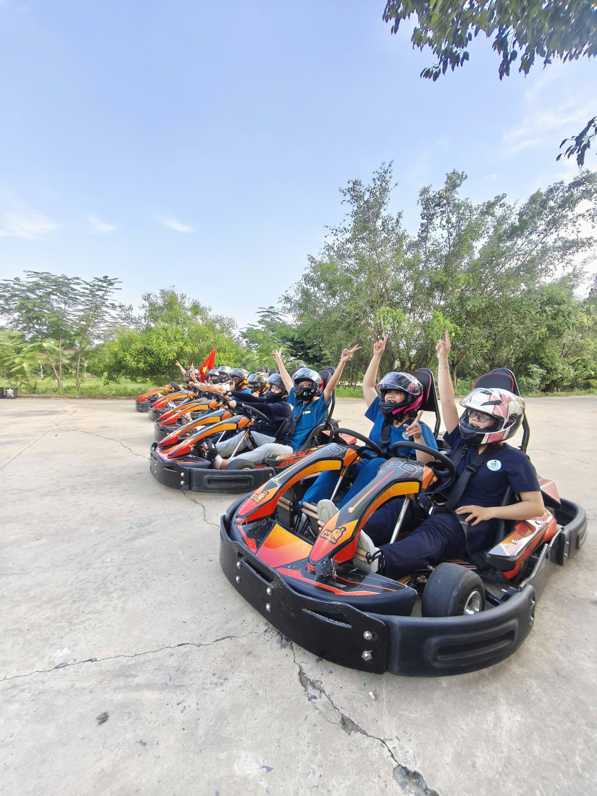 Đoàn xe go-kart xếp hàng trên đường đua, các tay đua giơ tay vẫy